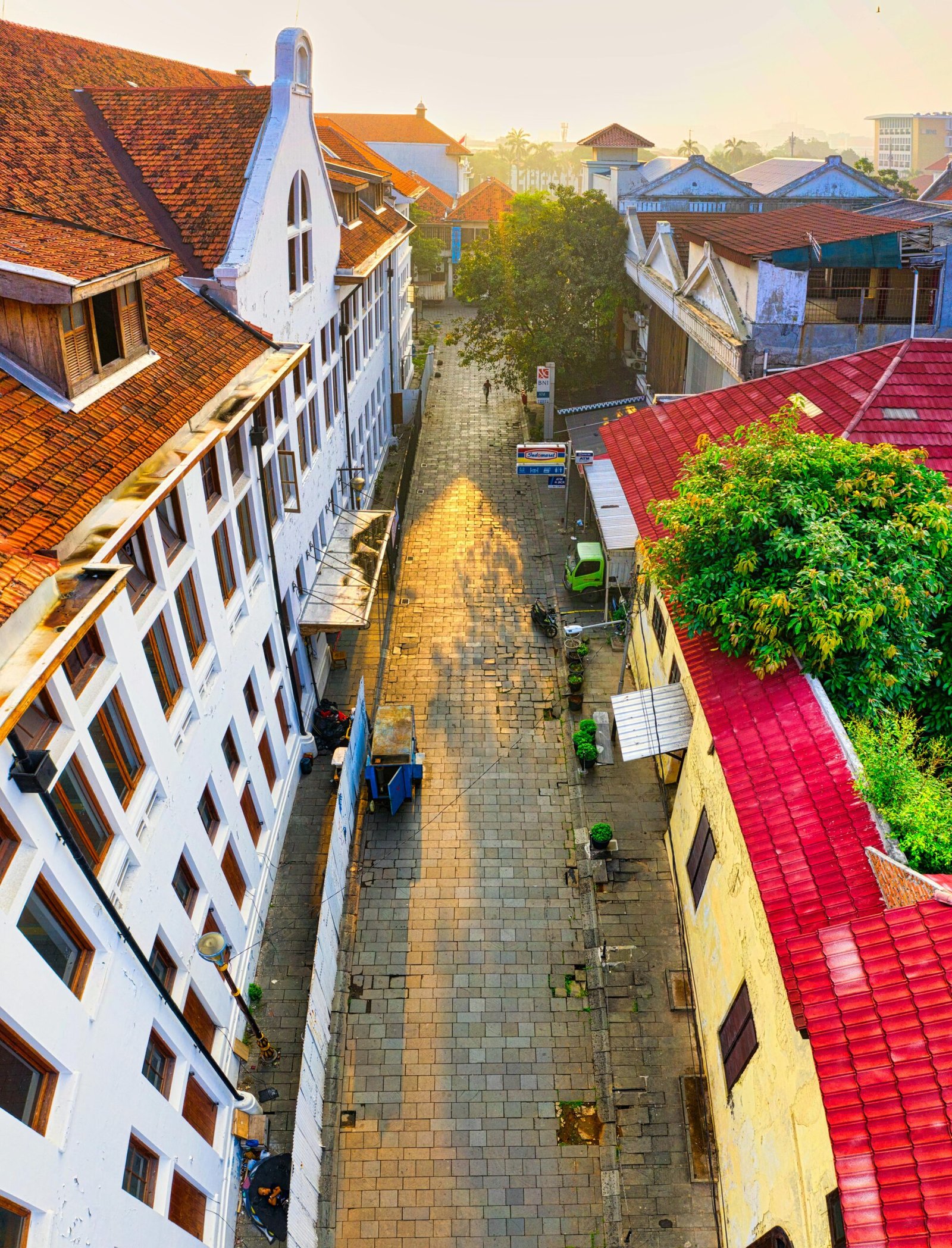 Historic Jakarta street captured from above at sunrise, showcasing traditional architecture and vibrant roofs.